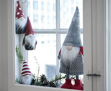 Božični škrat v sivi in rdeči barvi ter manjši škratki ob oknu
