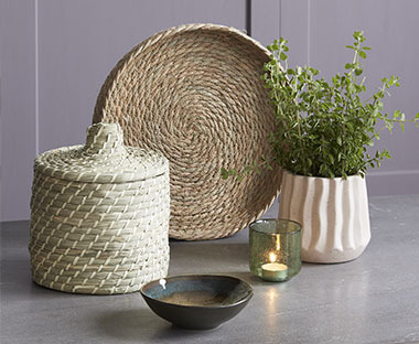 Pleten pladenj in pletena posodica s pokrovom ob cvetličnem lončku in keramični skodelici