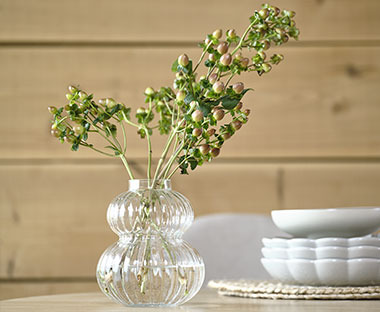 Steklena vaza in umetna rastlina ter sklede in krožniki