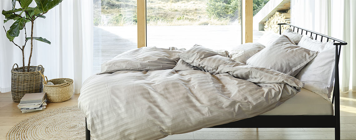 Spalnica črno kovinsko posteljo, prešitima odejama in vzglavnikoma s posteljnino s črtami