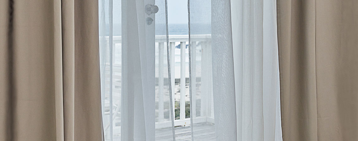 Pogled na balkon skozi odprta vrata s plapolajočimi zavesami