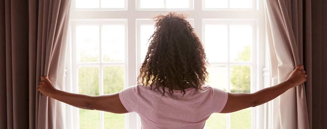 Ženska zagrinja izolacijske zavese prek svetlih belih oken
