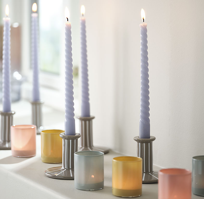 Svetlo modra sveča v svečniku z belimi črtami in svečniki za čajne svečke v modri, rumeni in rdeči barvi