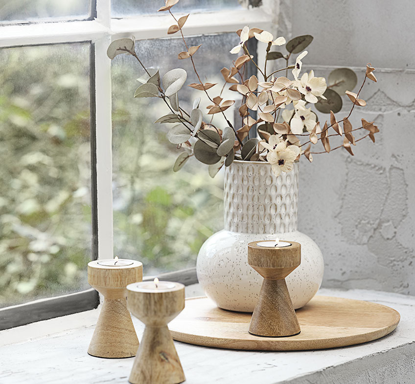 Svetlo bež ali bela reliefna vaza z umetnimi rožami in lesenimi svečniki za čajne svečke