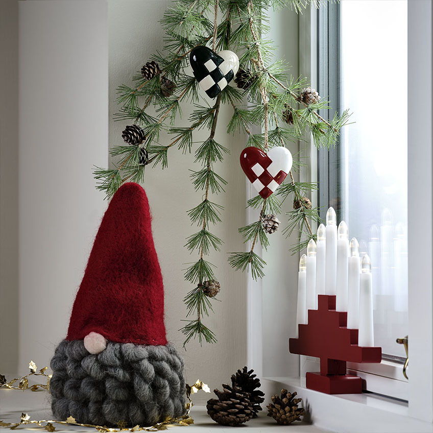 Božični škrat z rdečo kapo in sivo brado, rdeč svečnik z LED svečami in umetna zimzelena vejica