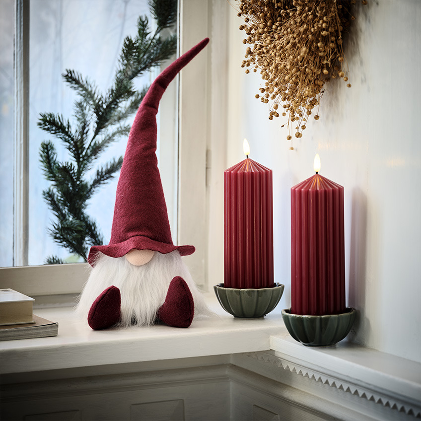 Skandinavski božični škrat na okenski polici ob velikih rdečih svečah