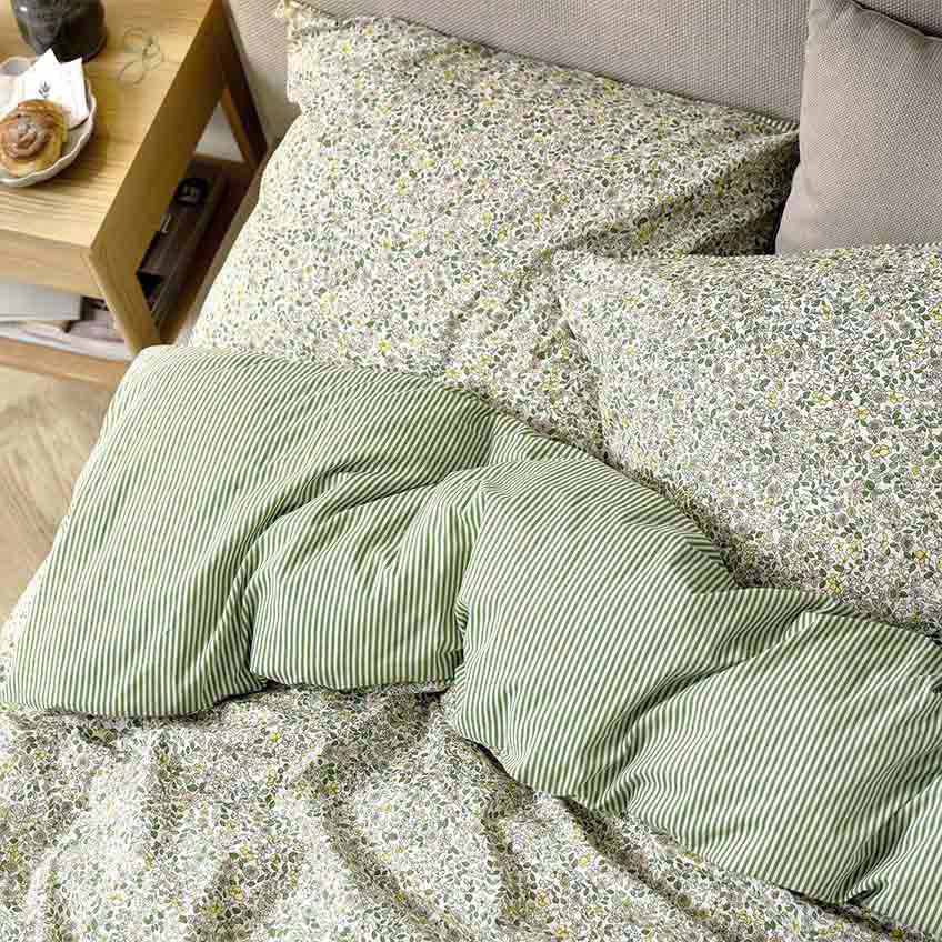 Postelja prekrita s posteljnino v zeleni barvi z malimi cvetlicami in črtasto drugo stranjo