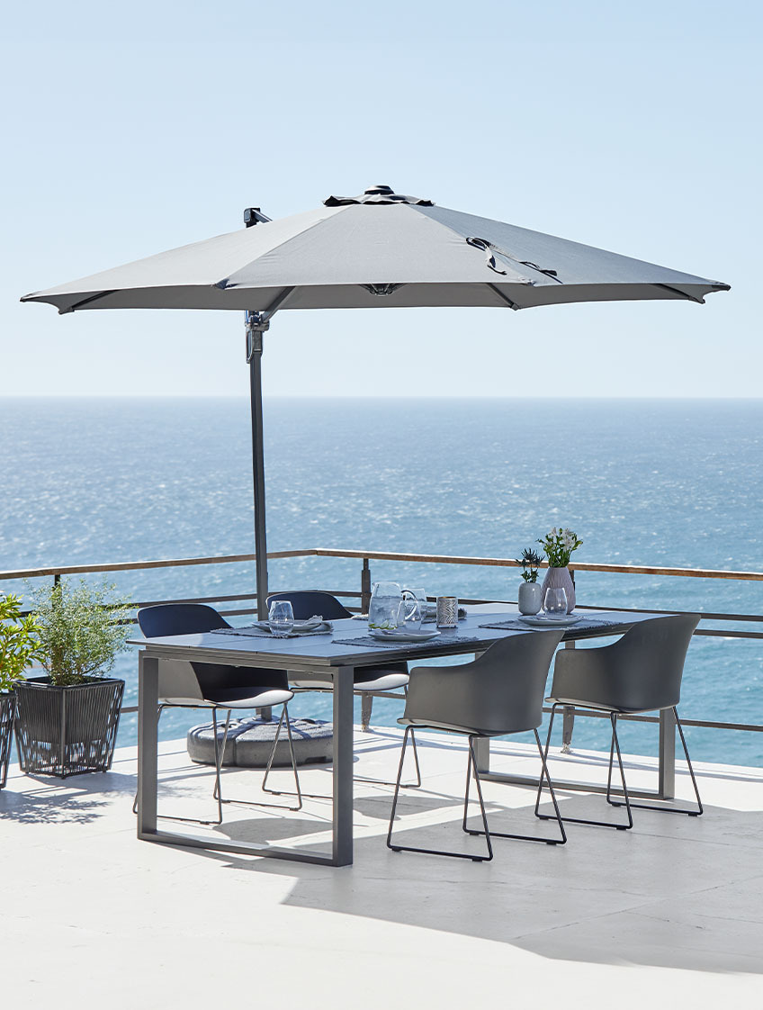 Velik viseč senčnik na terasi ob morju z vrtno mizo in vrtnimi stoli