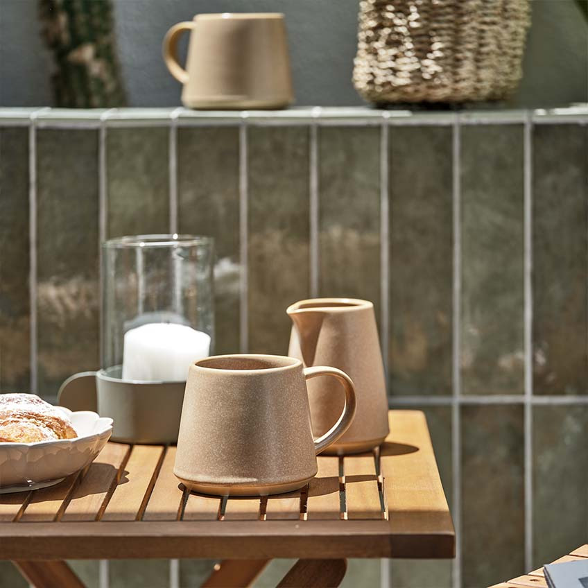Kavna skodelica in lonček za mleko na leseni vrtni mizi na balkonu