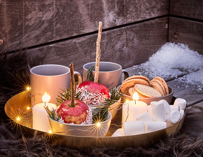 Skodelice čaja in sladic na pladnju na zimski terasi s svečkami