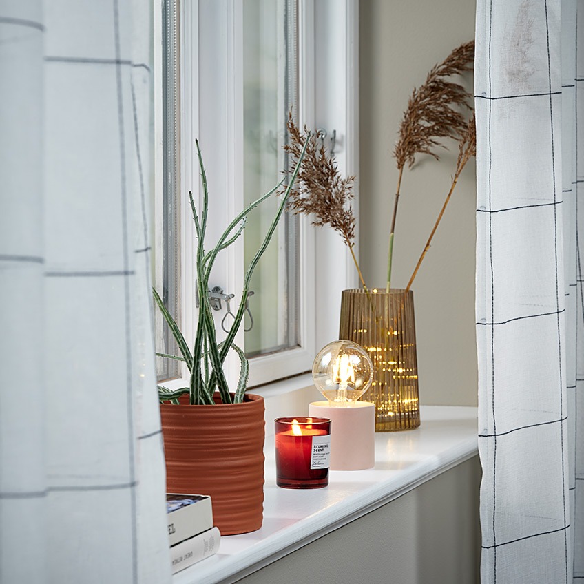 Lahke zavese na oknu s cvetličnim lončkom, dišečo svečo in svetilko na baterije na okenski polici
