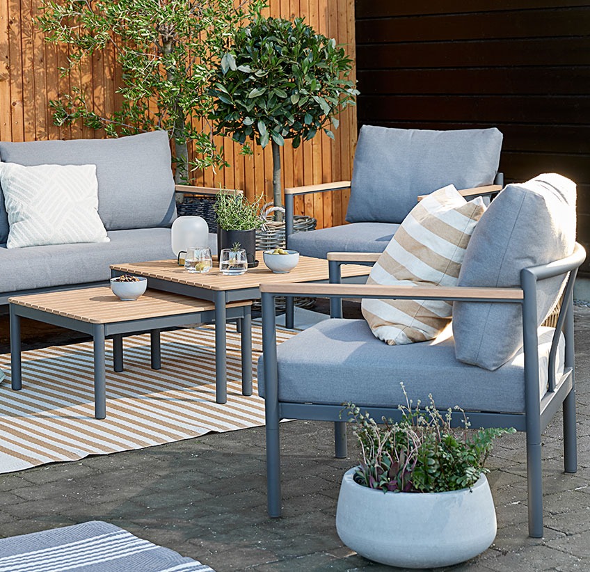 Vrtni lounge komplet z mehkimi blazinami na terasi s preprogo in cvetličnimi lonci