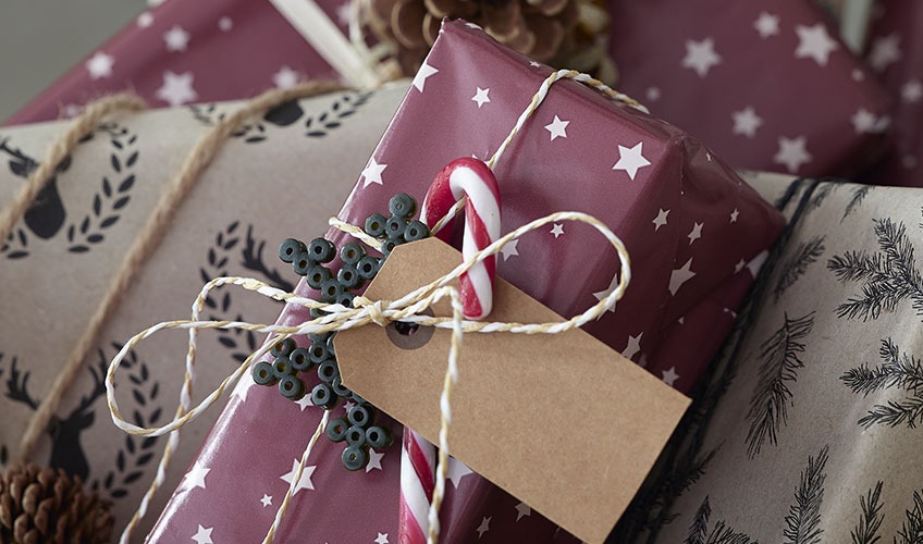 Božično darilo zavit v ovijalni papir in okrašen z liziko ter okraskom iz perl