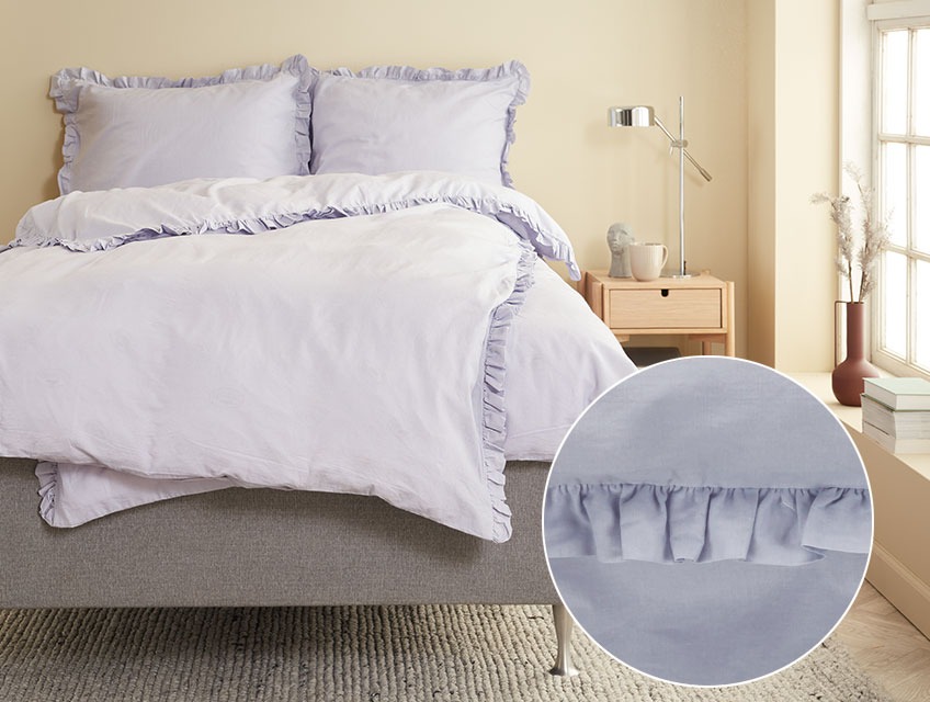 Postelja prekrita s posteljnino v vijolični barvi in naborki ob robu