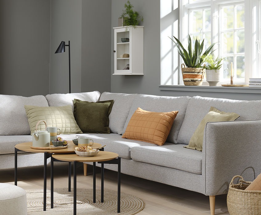 Dnevna soba s kavčem v sivi barvi ter okrasnimi blazinami v oranžni, sivi in zeleni barvi 