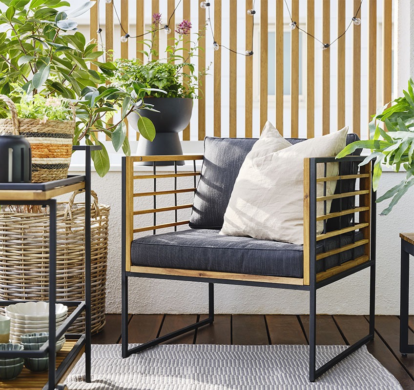 Balkon v vrtnim lounge stolom iz lesa in v črni barvi z mehkimi blazinami ter zelene rastline