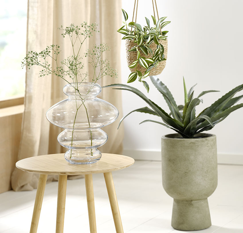 Steklena vaza na klubski mizi, viseč cvetlični lonček in zelen cvetlični lonček z umetno rastlino
