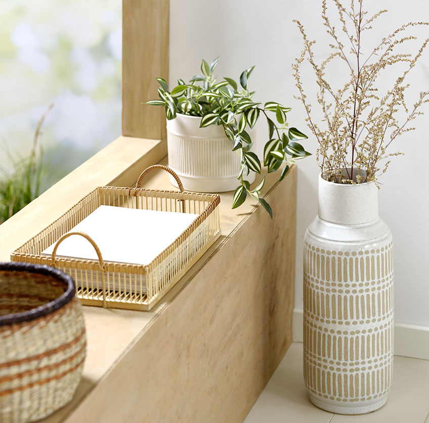 Visoka vaza pod okensko polico s pladnjem iz bambusa in belim cvetličnim lončkom z umetno rastlino