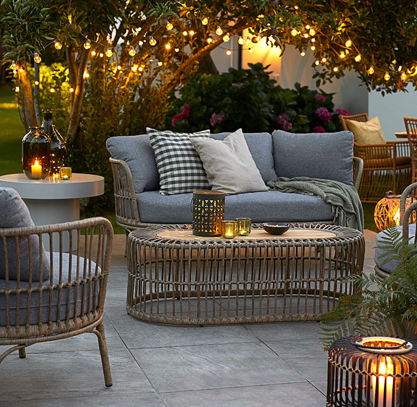 Udobna vrtna lounge garnitura na terasi z verigami lučk, baterijskimi svetilkami, lanternami ter svečniki s svečami