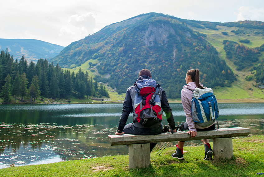 Moški in ženska sedita na klopi pred gorskim jezerom